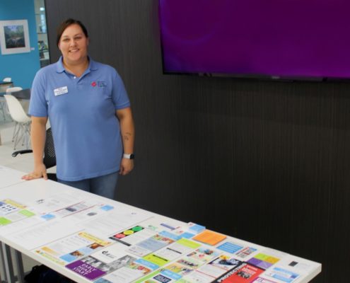 a woman in a blue shirt stands by a table with dozens of multi colored brochures